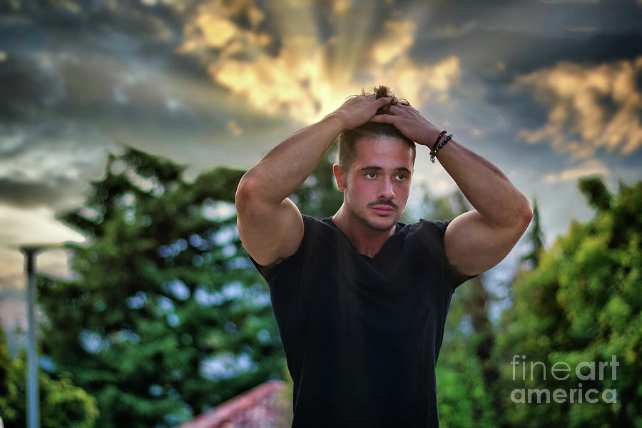 Handsome Muscular Man Sitting On Brick Wall Looking At Camera Wearing