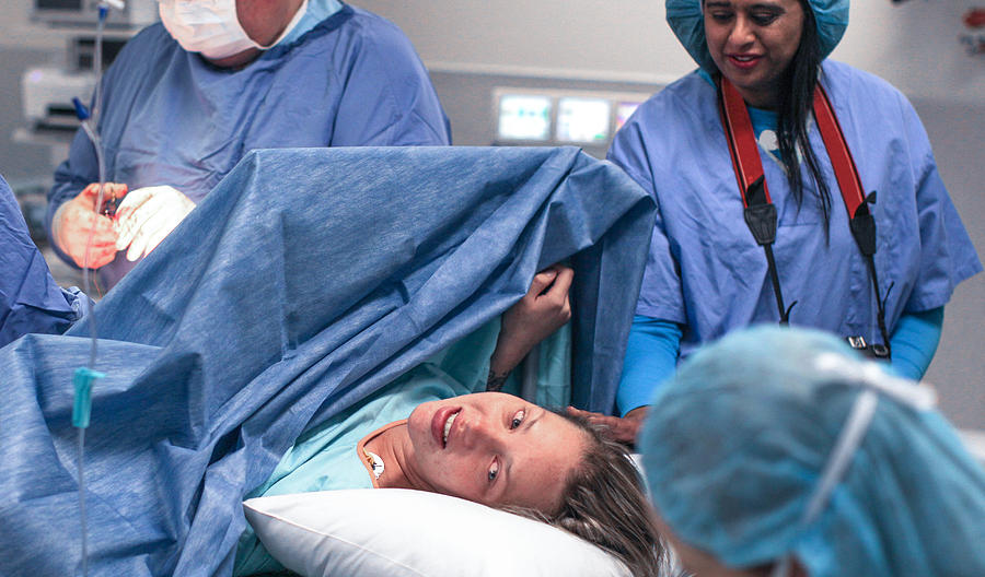 a Doula supports and comforts her emotional pregnant client as she lays in the operating theatre. #1 Photograph by Petri Oeschger