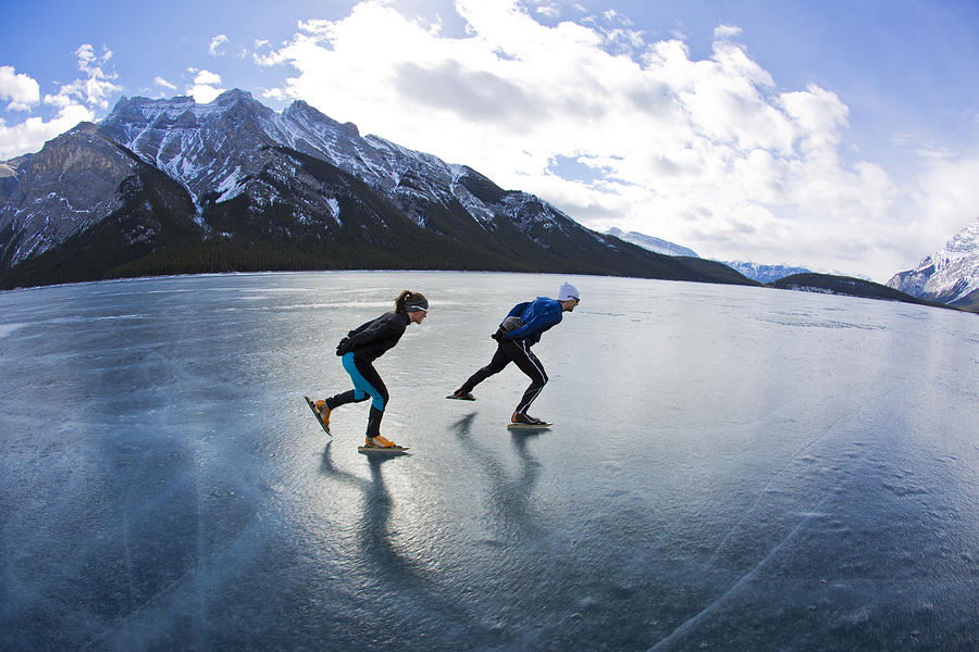 A man leads a woman on a winter speed skating adventure on Lake Minnewanka in Banff National Park, Alberta, Canada. #1 Photograph by GibsonPictures