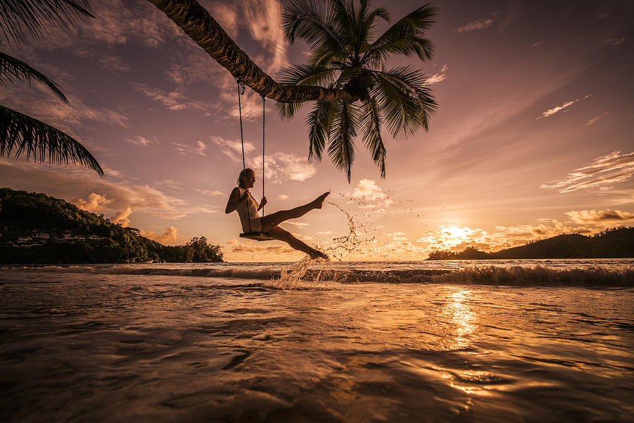Carefree woman swinging above the sea at sunset beach. #1 Photograph by BraunS