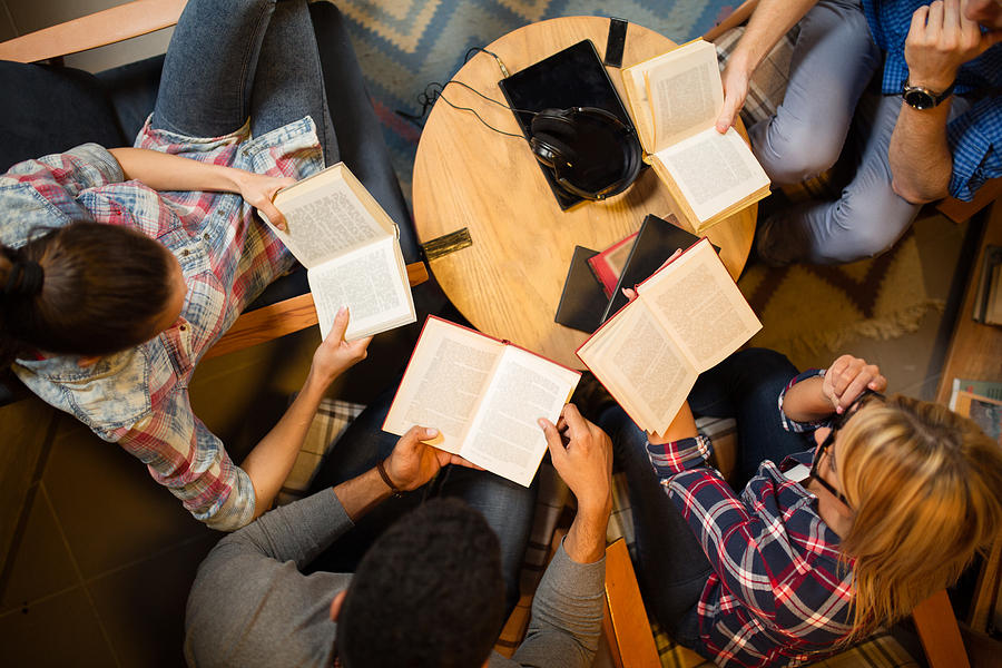 Diverse group of friends discussing a book in library. #1 Photograph by EmirMemedovski