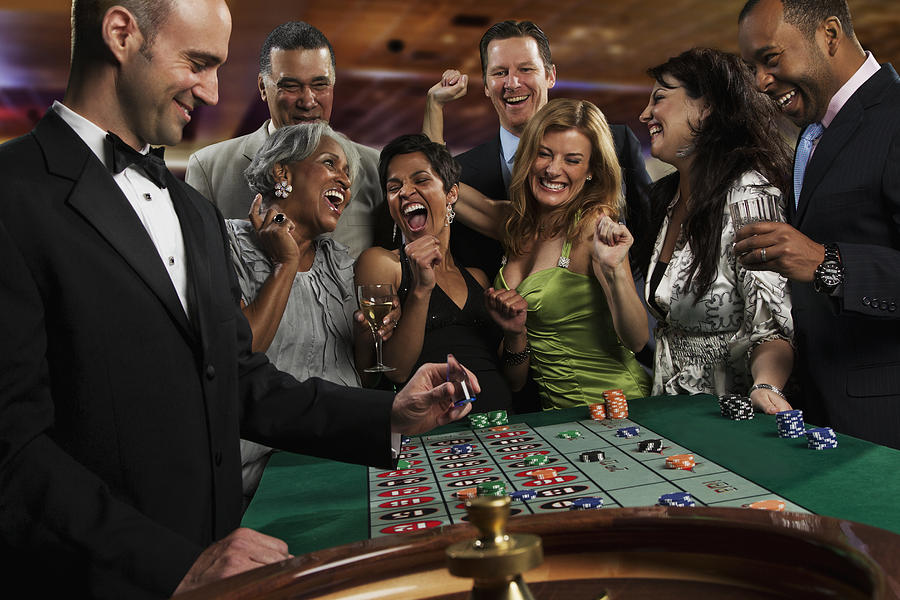 Excited friends gambling at roulette table in casino #1 Photograph by Jon Feingersh Photography Inc