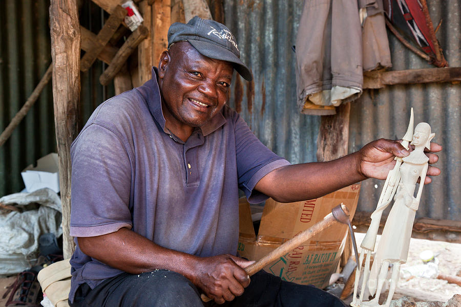 Kenya. December 10th. A man carving figures in wood. #1 Photograph by  Michal Bednarek - Pixels
