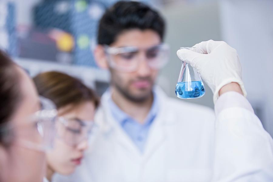 Lab Assistants Looking At Flask Photograph by Science Photo Library