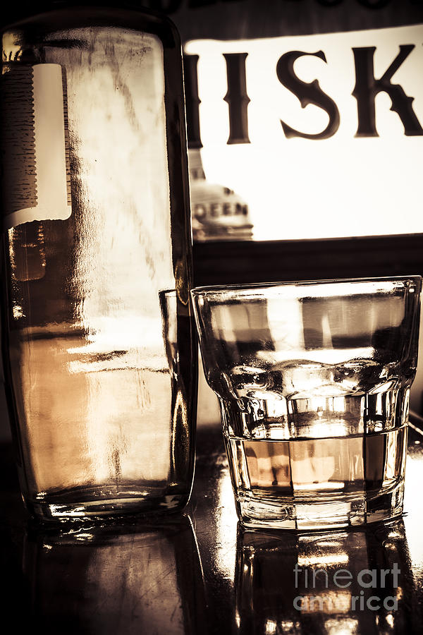 Liquor bottle beside spirit glass on dark bar top #1 Photograph by Jorgo Photography