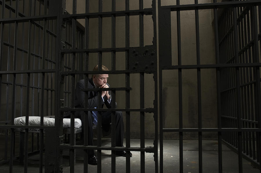 Mature businessman sitting on bed in prison cell Photograph by Darrin Klimek