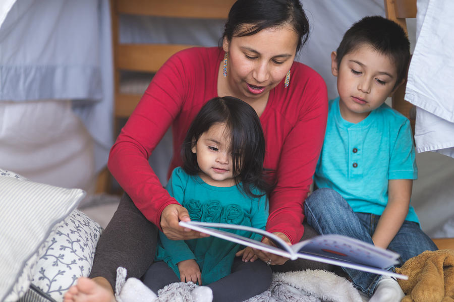 Native American mom reads with her two children under makeshift fort in living room #1 Photograph by FatCamera