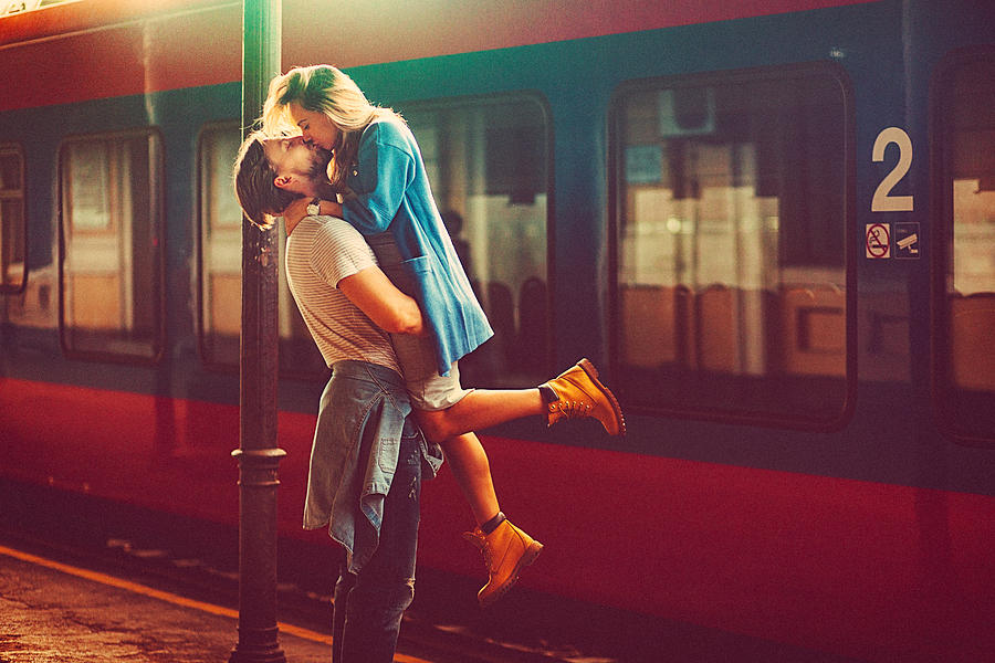 Passionate young man and woman kissing beside the train at the railway station #1 Photograph by Gruizza