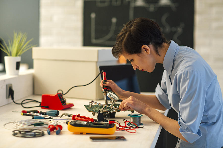 Woman Soldering a circuit board in her tech office. #1 Photograph by Vgajic