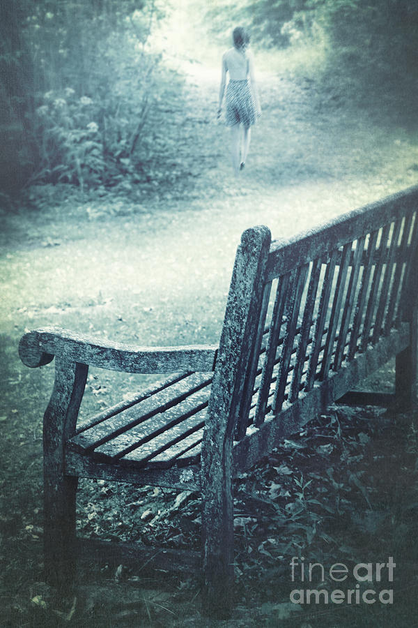 Wooden bench in a park with woman walking away #1 Photograph by Sandra Cunningham