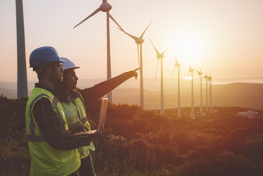 Young maintenance engineer team working in wind turbine farm at sunset #1 Photograph by Serts