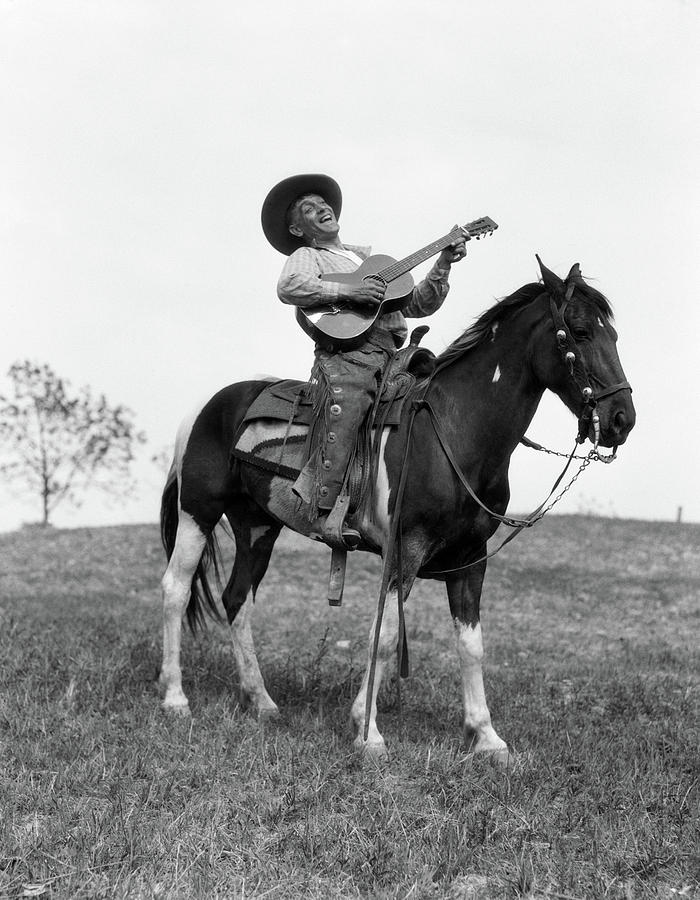Black And White Photograph - 1920s Cowboy On Horse Singing & Playing by Vintage Images