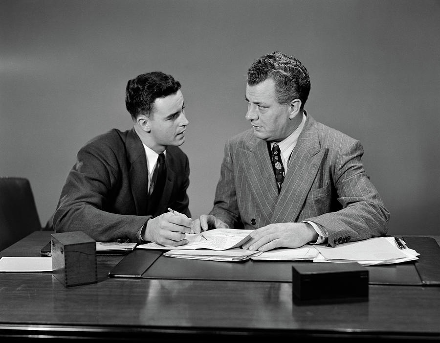 Black And White Photograph - 1940s Two Men Seated Desk Looking by Vintage Images