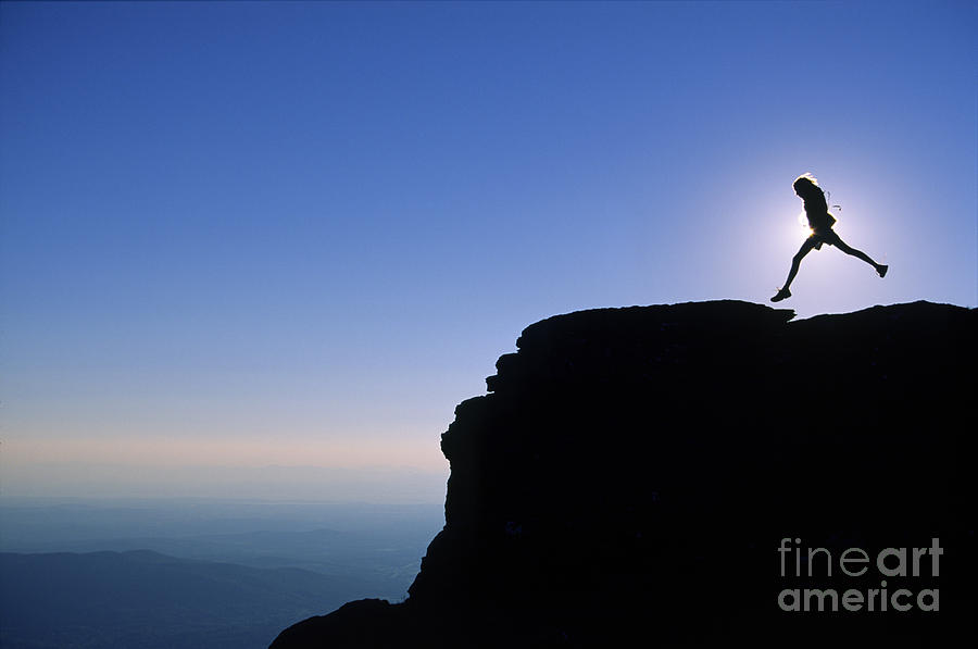 Silhouette of a girl jumping over a rock cliff. Photograph by Don ...