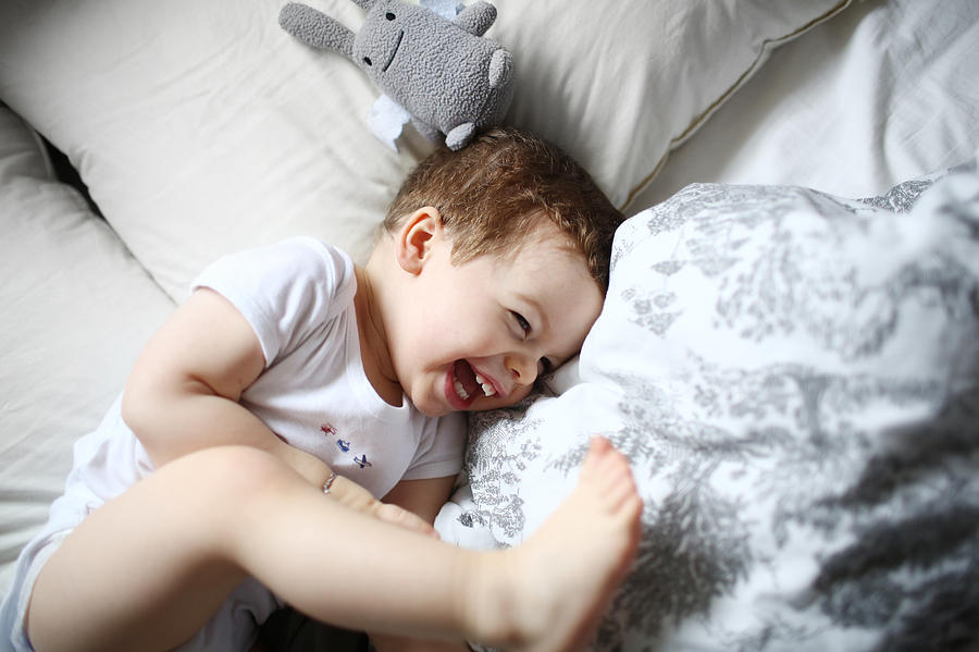 A 2 years old boy laughing in a bed Photograph by Catherine Delahaye