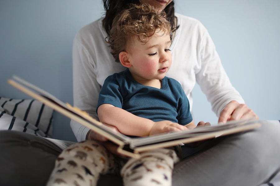 A 2 years old boy reading a book with his mom Photograph by Catherine Delahaye