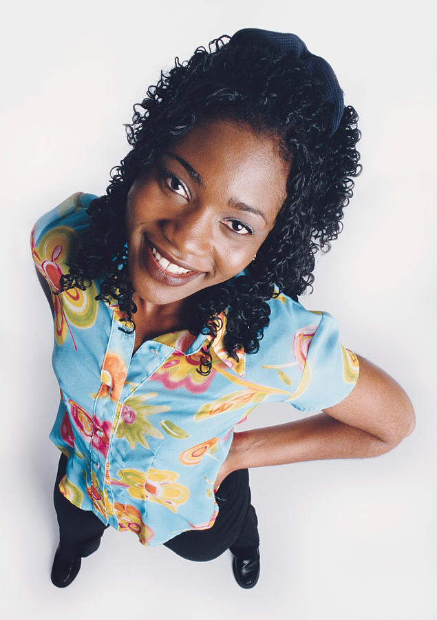 A Beautiful African American Young Woman With Curly Long Hair Is Wearing A Blue Floral Blouse And Smiling Up At The Camera With Her Hands On Her Hips Photograph by Photodisc