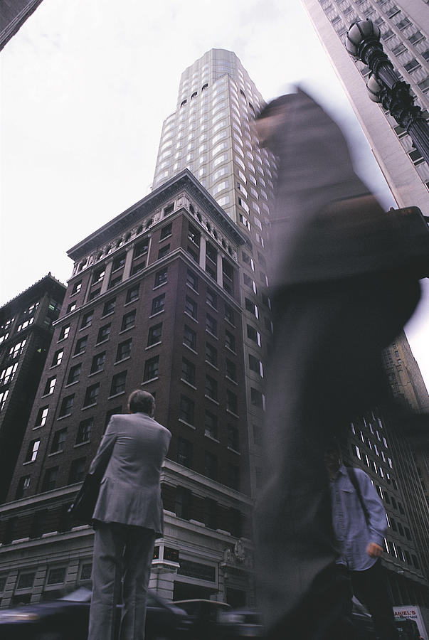 A Blurred Man Walks Past Others On A Road Amongst Skyscrapers Photograph by Photodisc