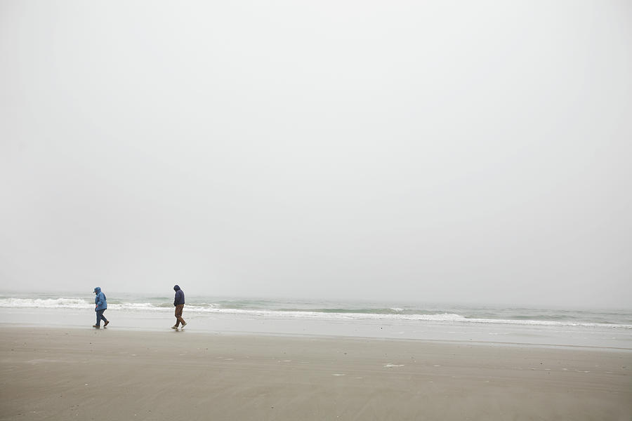 Beach Photograph - A Couple Walks On The Shore Of A Foggy by Eyeconic Images