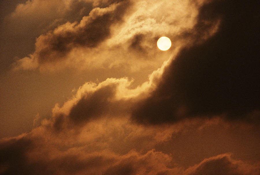 A Full Moon Peaks Out From Behind A Cloud Covering With A Warm Glow Photograph by Rubberball