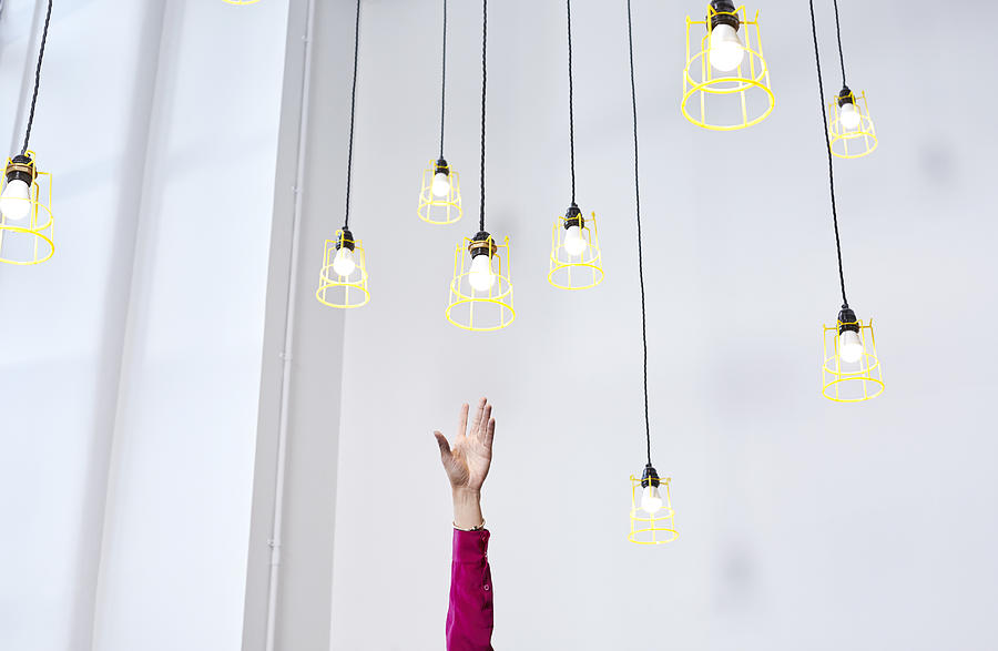 A hand reaching for conceptual idea lightbulbs Photograph by Ezra Bailey
