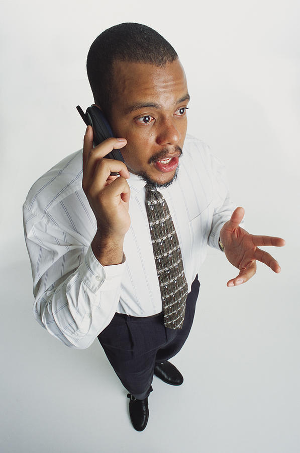 A Handsome Young African American Man In A White Shirt And Dark Slacks Talking Into A Cell Phone Photograph by Photodisc
