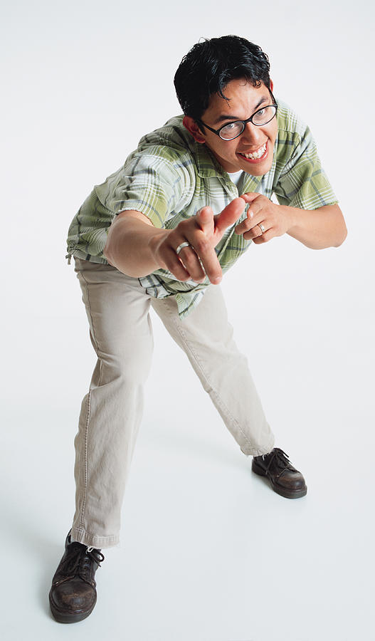 A Latino Young Man Is Standing Bent Forward Looking At The Camera As He Points With Both Hands Towards The Camera And Smiles Photograph by Photodisc