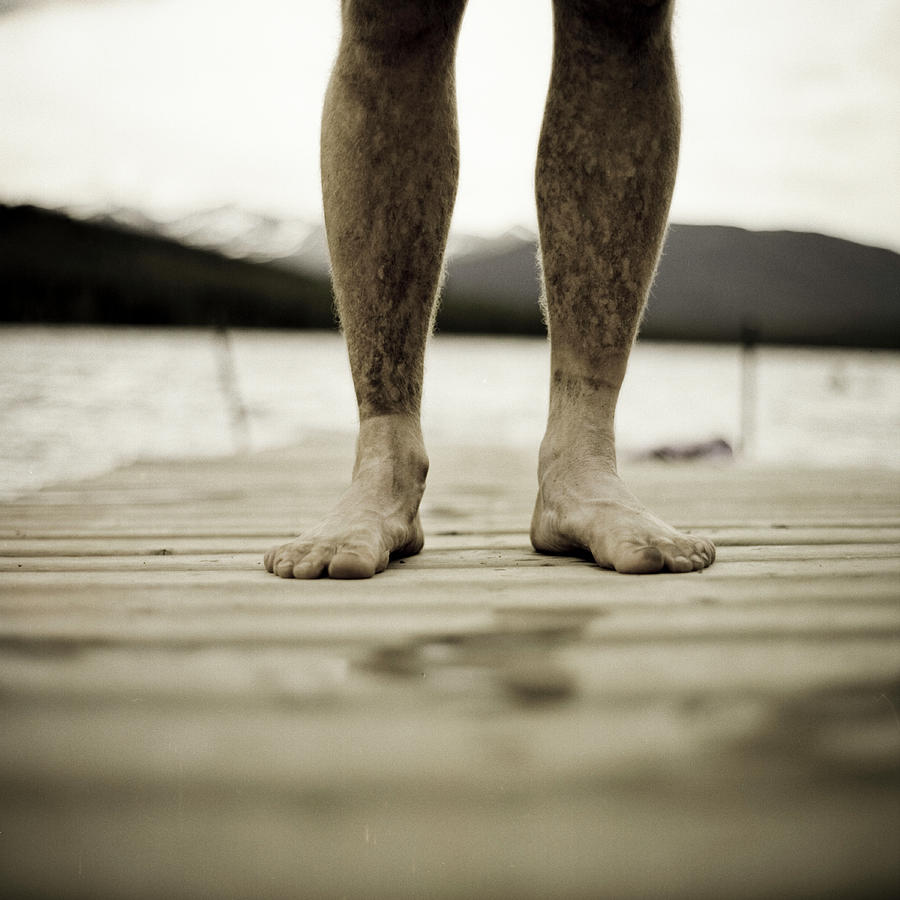 Pier Photograph - A Man Stands On A Dock With Clean Feet by Kari Medig
