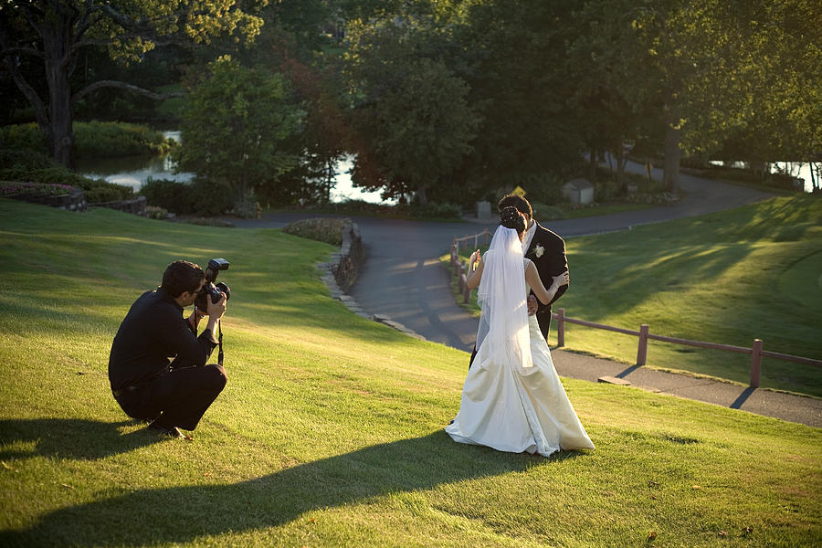 A man taking a photo of a bride and groom missing in grass Photograph by Zxvisual