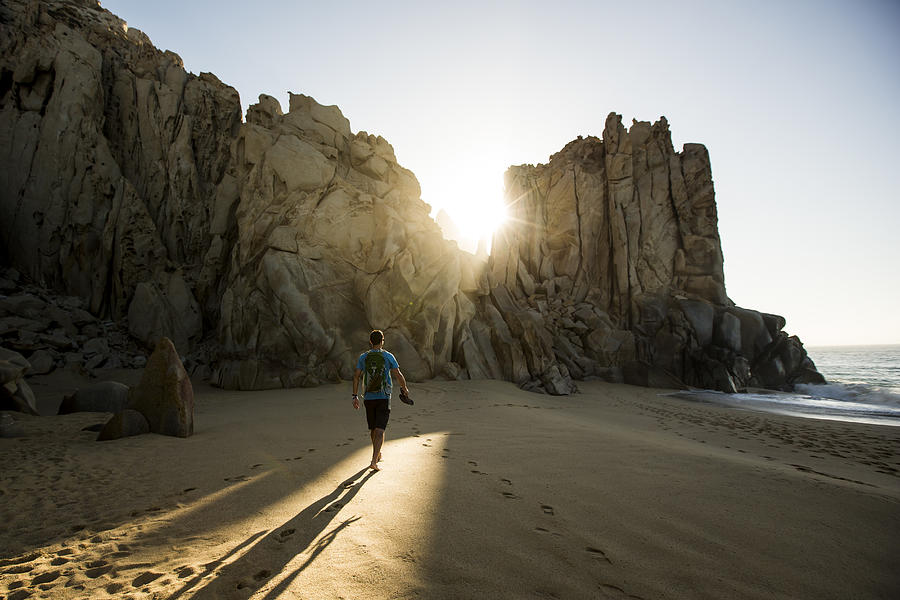 A man walking a beach at sunrise. Photograph by Jordan Siemens