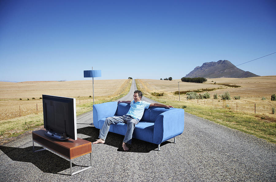 A man watching television on a couch in the road Photograph by OJO Images