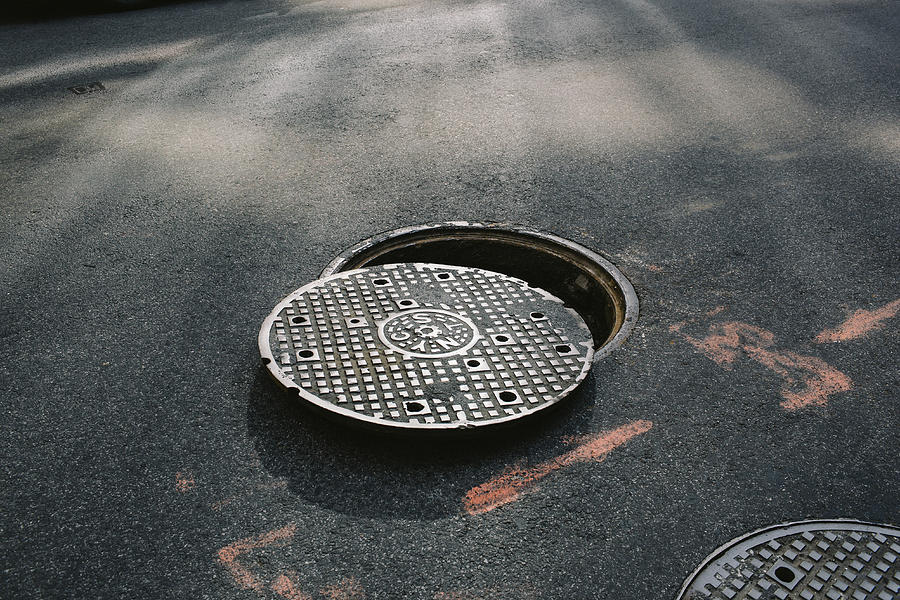 A manhole cover partially removed, close-up Photograph by Peter Baker