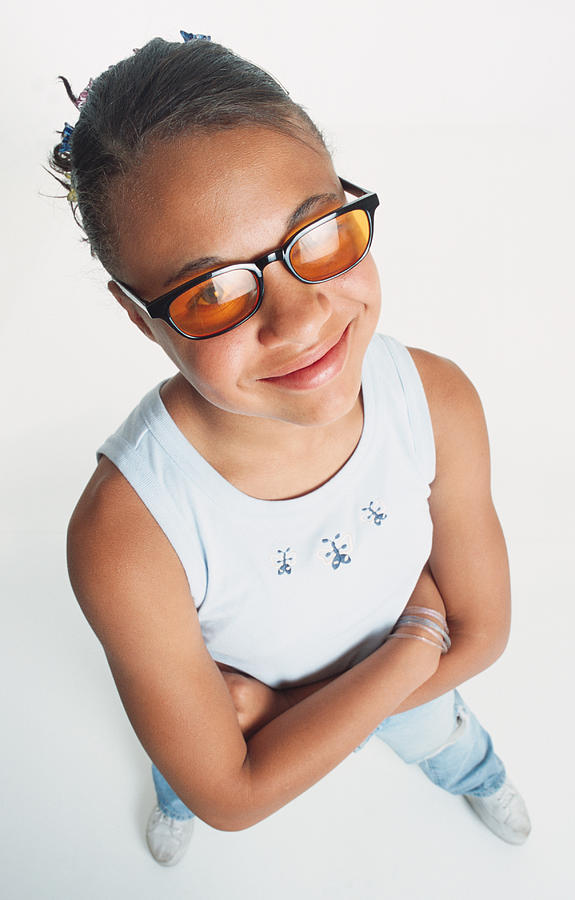A Pretty African American Pre Teen Girl In A White Tank Top Is Wearing Orange Sunglasses And Has Her Hair Pulled Back As She Looks Up At The Camera Grinning Photograph by Photodisc