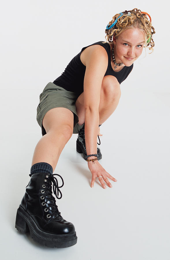 A Pretty Caucasian Teenage Girl With Long Blond Dreadlocks Pinned Up On Her Head Wears Army Boots And Shorts As She Strikes A Pose While Squatting Photograph by Photodisc