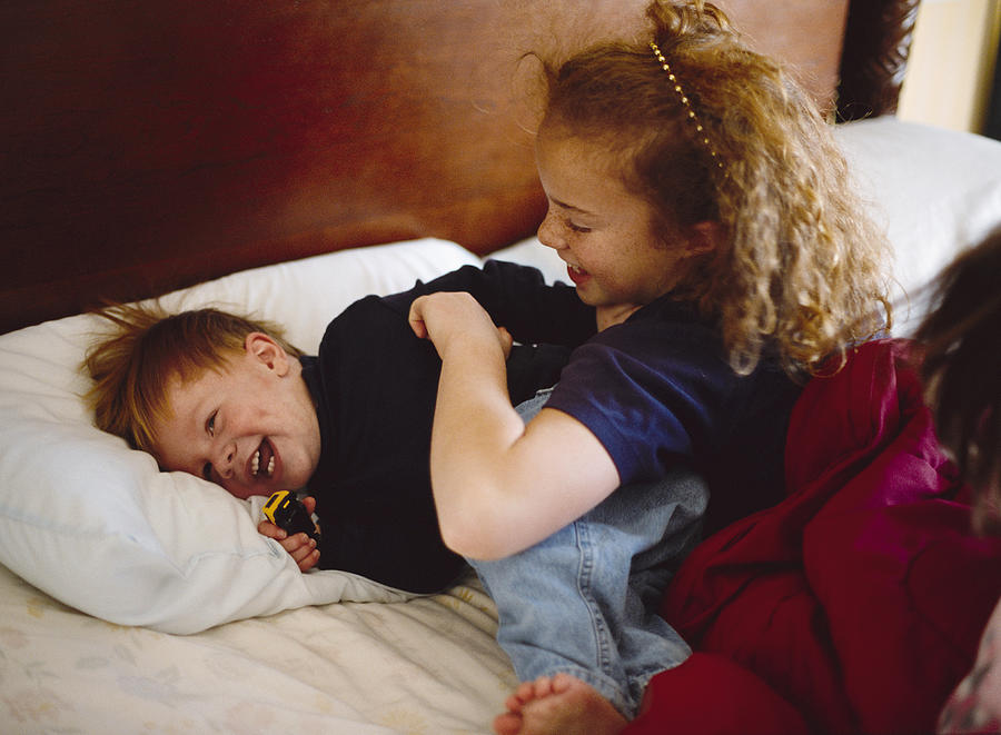 A redhaired big sister tickles her little brother on a bed Photograph by Photodisc