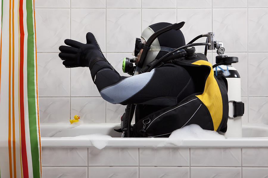 A scuba diver sitting in a bathtub preparing to dive in Photograph by Twins