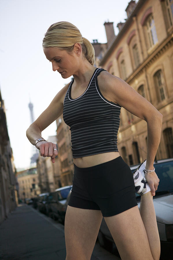 A Young Caucasian Blonde Woman In A Black Running Outfit Stretches And Checks Her Watch On The Streets Of Paris Photograph by Photodisc