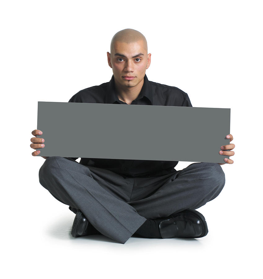 A Young Hispanic Male In Grey Slacks And A Black Shirt Sits Cross-legged On The Floor As He Holds A Blank Sign On His Lap With Both Hands And Looks Straight Ahead At The Camera Photograph by Photodisc