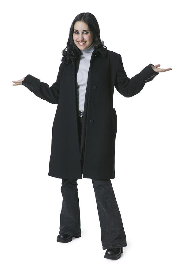 A Young Hispanic Woman In A Long Black Coat Smiles As She Shrugs Her Shoulders Photograph by Photodisc
