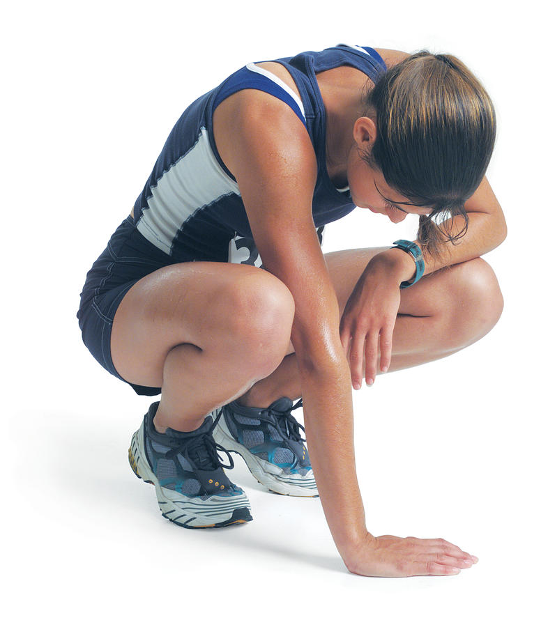 A Young Woman In A Blue Track Uniform Is Squatting Down As She Leans Against Her Knee And Looks Down Photograph by Photodisc