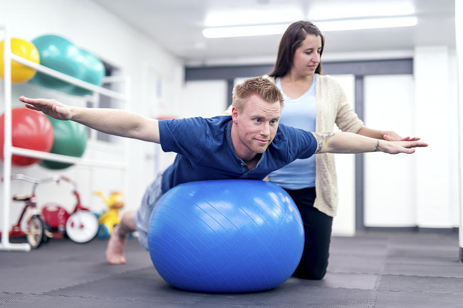 Adult male patient balancing on a therapy exercise ball Photograph by FatCamera