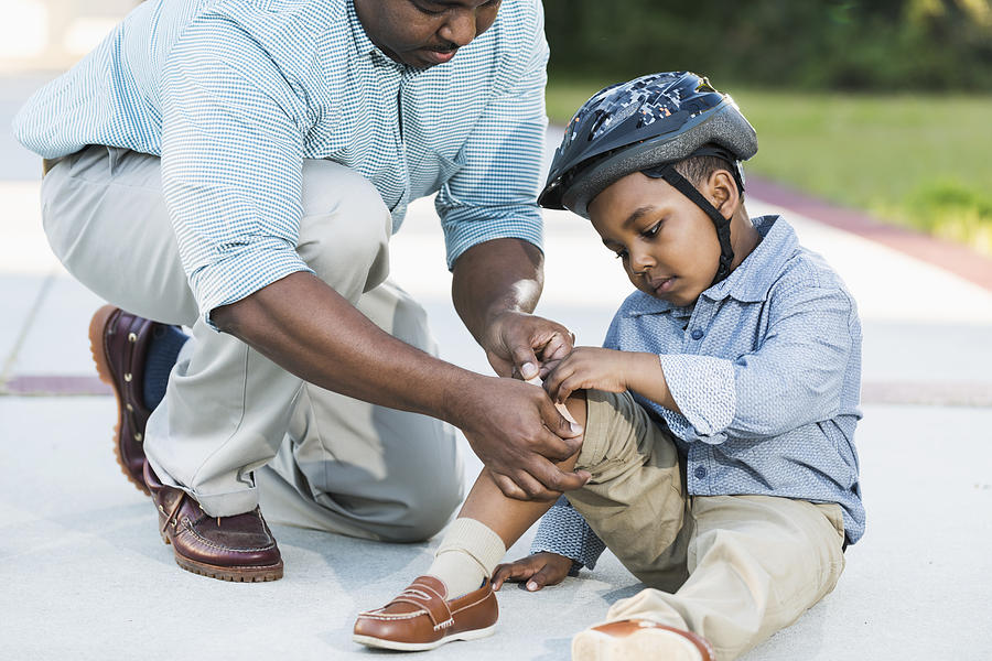 African American father putting bandage on sons knee Photograph by Kali9