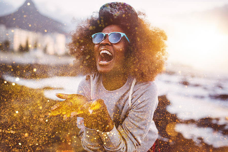Afro hipster girl laughing ecstatically while throwing gold glitter Photograph by Wundervisuals