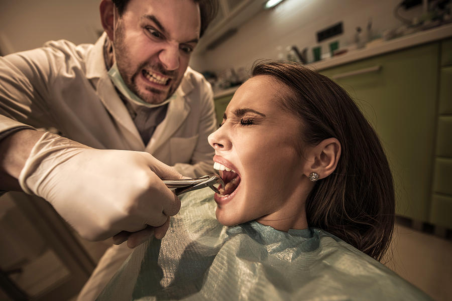 Aggressive dentist about to take out womans tooth. Photograph by BraunS