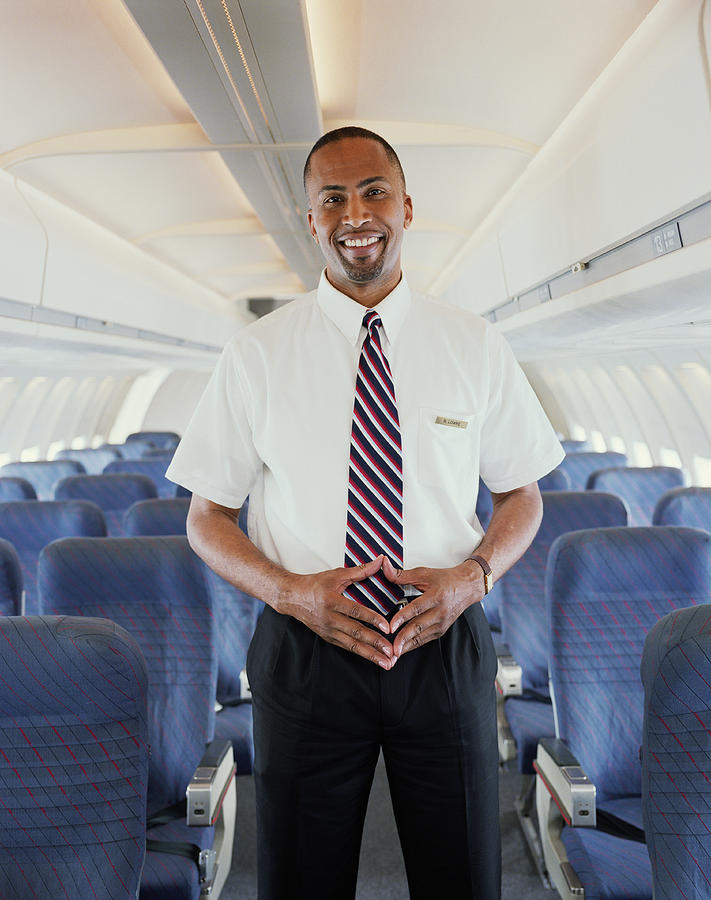 Air steward standing in aisle of aeroplane, smiling, portrait Photograph by Digital Vision