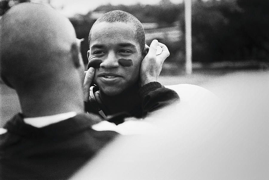 American footballer painting team-mates face, outdoors (B&W) Photograph by Doug Menuez / Forrester Images
