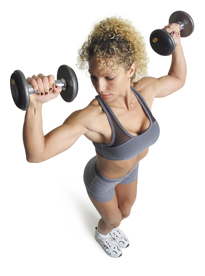 An Adult Caucasian Female In Grey Shorts And Sports Bra Works Out By Lifting Dumbell Weights Up And Above Her Head Photograph by Photodisc