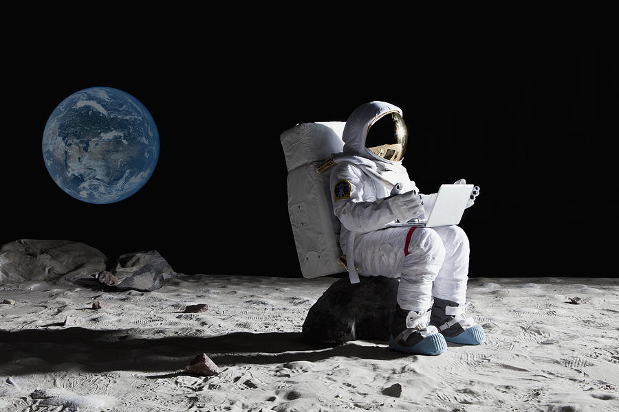 An astronaut on the moon sitting on a rock using a laptop Photograph by fStop Images - Caspar Benson