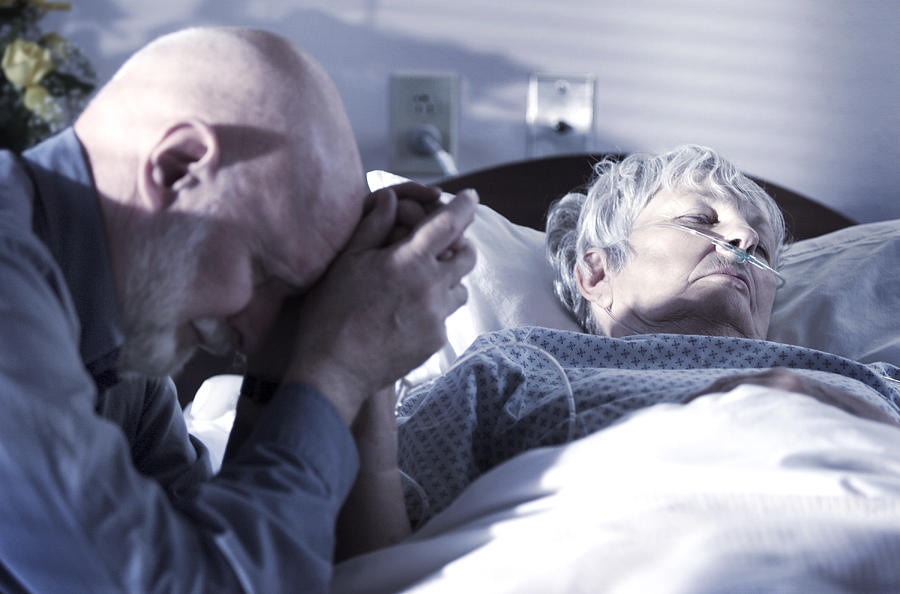 An Elderly Caucasain Gentleman Visits And Prays Over His Wife As She Tries To Recover From An Illness Photograph by Photodisc