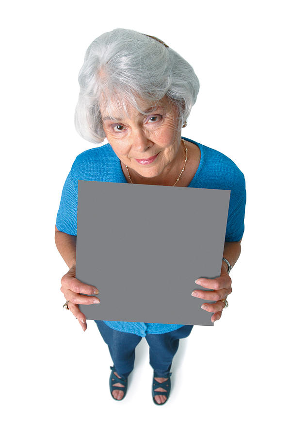 An Elderly Caucasian Woman In A Blue Shirt Holds A Sign In Front Of Her As She Smiles Up At The Camera Photograph by Photodisc